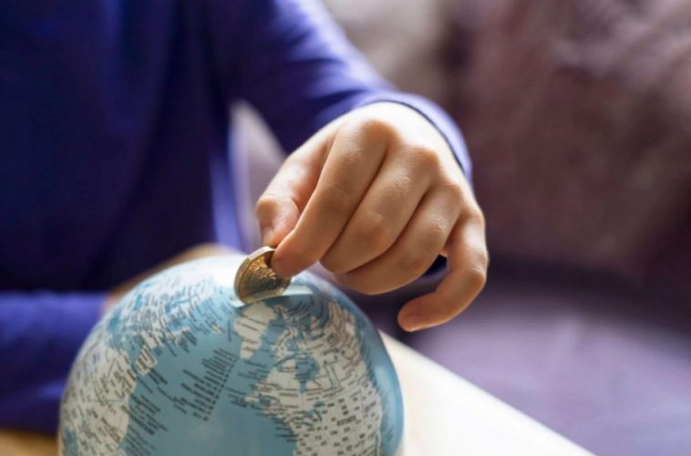 Kid hand putting one pound coin into piggy bank to donate money